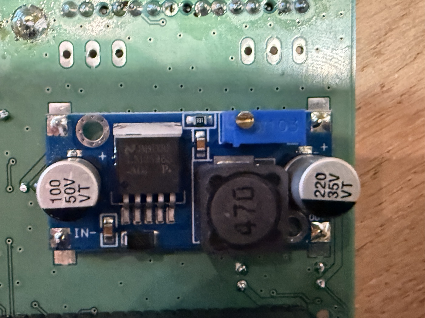 DC-DC step-down daughterboard inside Magic Box v1.4 — IN- pad labeled on the left side (input, raw battery voltage); the right side, near the motherboard edge, has the 5 V regulated output pads